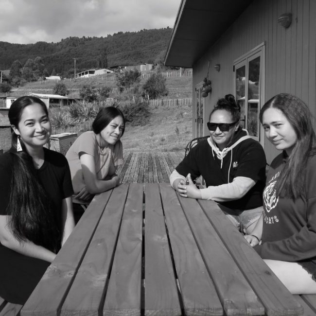 Staff Seated With Momi Afelin Of Hawaii At Table Outside Manawa Honey Office, Ruatāhuna, Te Urewera, NZ Three Women Staff Seated With Momi Afelin Of Hawaii At Table Outside Manawa Honey Office, Ruatāhuna, Te Urewera, NZ