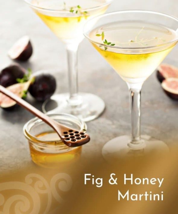 A close-up of two elegant martini glasses filled with a golden Fig & Tawari Honey Martini, garnished with a sprig of thyme. Fresh figs and a small jar of honey with a honey dipper are artfully arranged nearby.
