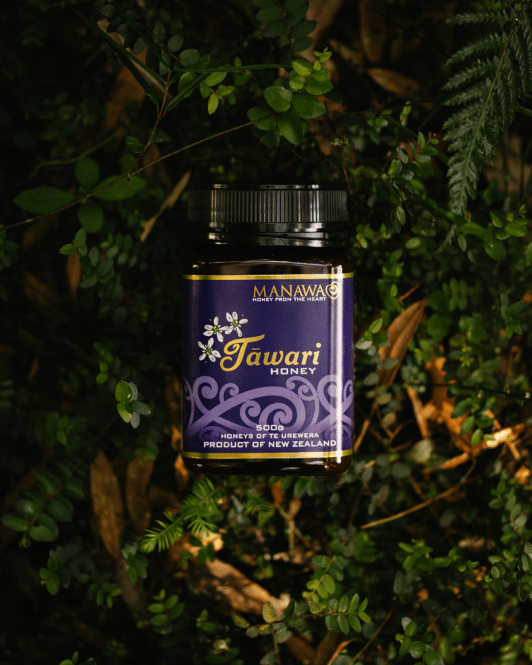 Creamed Tawari Honey from Manawa Honey NZ, award-winning honey jar surrounded by native New Zealand foliage.